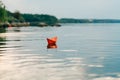 A paper boat sails by the river in the summer. It has an orange color and floats downstream along the shore Royalty Free Stock Photo