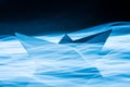 Paper boat splitting blue light trails symbolizing waves in the sea