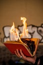 Paper book burns to ashes, on concrete tiles, manuscript burns, open book with fire in man hand Royalty Free Stock Photo