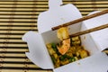 Paper box with pad thai on a bamboo mat. Chopsticks with shrimp