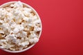 Paper bucket with delicious popcorn on red background, top view. Space for text Royalty Free Stock Photo