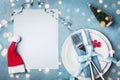 Paper card, white plate and cutlery decorated santa hat and small fir tree. Magic christmas table setting top view. Copy space. Royalty Free Stock Photo
