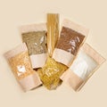 Paper-cellophane bags with cereals, legumes and pasta laid out on beige backdrop. Top view