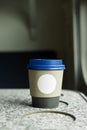 A paper coffee cup with a blue plastic lid and a white inscription circle