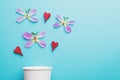 Paper coffee cup, butterflies made of fresh flower petals and red wooden hearts isolated on pastel blue background, copy space Royalty Free Stock Photo