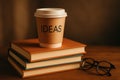 Paper coffee cup with IDEAS text on stack of books next to eyeglasses, warm brown background, creative thinking concept. Royalty Free Stock Photo
