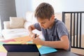 Education, paper crafts for kids. Child cutting colored paper with scissors. Boy looking video tutorial and making paper