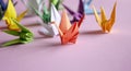 Paper cranes - origami on a pink background. Do-it-yourself jewelry. On the table are colored cranes made of paper