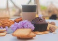 Paper cup with assorted pastries, chocolate muffin and lilac flowers, outdoor