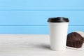 Paper cup with black lid and muffin on white wooden table, space for text. Coffee to go Royalty Free Stock Photo