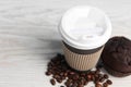 Paper cup, coffee beans and muffin on white wooden table, closeup with space for text. Coffee to go Royalty Free Stock Photo