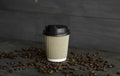 Paper cup of coffee with roasted coffee beans on wooden table background. Mug of black coffee.