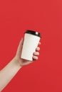 Paper cup of coffee or tea on a red background. Mockup of male hand holding paper cup isolated. Front view mockup of empty Royalty Free Stock Photo