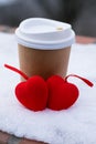 Paper cup for coffee to go and decorative red hearts on the snow in winter. Concept of serious relationship and valentine`s day Royalty Free Stock Photo