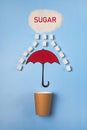 A paper cup is covered with a sugar rain umbrella on a blue background. The concept of reducing or giving up sugar. Tea or coffee