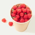 Paper cup filled with vibrant red raspberries, minimalist presentation