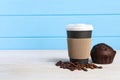 Paper cup with plastic lid, coffee beans and muffin on white wooden table, space for text. Coffee to go Royalty Free Stock Photo