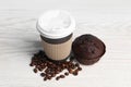 Paper cup with plastic lid, muffin and coffee beans on white wooden table. Coffee to go Royalty Free Stock Photo