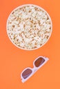 Paper cup with popcorn and 3D glasses on orange background, top view. Flat lay