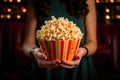 Paper cup with popcorn in the hands of a woman in a movie theater close-up