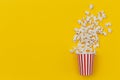 Paper cup with spread popcorn on color Popcorn viewed from above on yellow background. Cinema snack top view