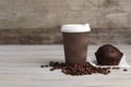 Paper cup with white lid, coffee beans and muffin on wooden table, space for text. Coffee to go Royalty Free Stock Photo