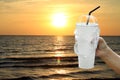 Paper cup white and straws in hand over sea beach sunset evening, fast food cup plastic for water drink is pollution waste ocean Royalty Free Stock Photo