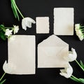 Paper envelop, white cards and flowers on black background. Flat lay, top view. Creative valentines day concept