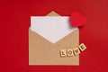 Paper envelope with a white sheet for text on a red background with hearts and the word `love` in wooden letters. Greeting card co Royalty Free Stock Photo