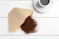 Paper filter, ground coffee and cup of drink on white wooden table, flat lay Royalty Free Stock Photo