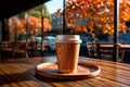 Paper green coffee or tea cup with wooden print, mockup for logo, on a wooden table in a cafe on the terrace in autumn