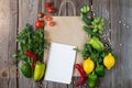 Paper grocery bag with blank notebook and fresh vegetables and fruits on wooden table top view. Eco shopping concept and product Royalty Free Stock Photo