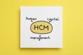 Paper with hCM abbreviation and its interpretation Human Capital Management on yellow background, top view