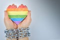 Paper heart painted in LGBT colors in the hands of a woman tied in chains