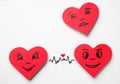 Paper hearts with drawn faces on background, top view. Concept of jealousy