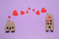 Paper hearts between two wooden house models on violet background symbolizing connection in long-distance relationship, flat lay