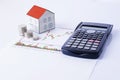 Paper house with coins and calculator on stock chart report