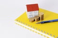 Paper house with coins stack with blue pen on yellow book