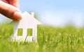 Paper house in green grass over blue sky