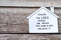 Paper house with a handwritten biblical verse on a wooden background