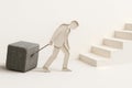 A paper man pulls a heavy stone cube to the stairs. Royalty Free Stock Photo