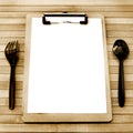 Paper menu with black plastic fork and spoon juxtapose on a wooden table have space, vintage style