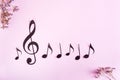 Paper musical clef and notes in a row and dried flowers on a pink background. Top view