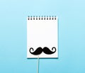 Paper mustache and a notepad on blue background. Royalty Free Stock Photo