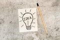 A paper note with a drawing of a light bulb with idea single word inside and a pencil on a gray stone background Royalty Free Stock Photo