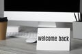 Paper note with phrase Welcome Back on office desk