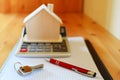 Paper notebook with calculator, house model, keys and pen on wooden table. Royalty Free Stock Photo