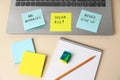 Paper notes with life-affirming phrases and laptop on white table, above view