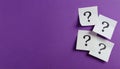 Paper notes with question marks on Violet background, flat lay. Space for text Royalty Free Stock Photo