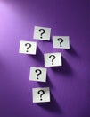 Paper notes with question marks on Violet background, flat lay. Space for text Royalty Free Stock Photo
